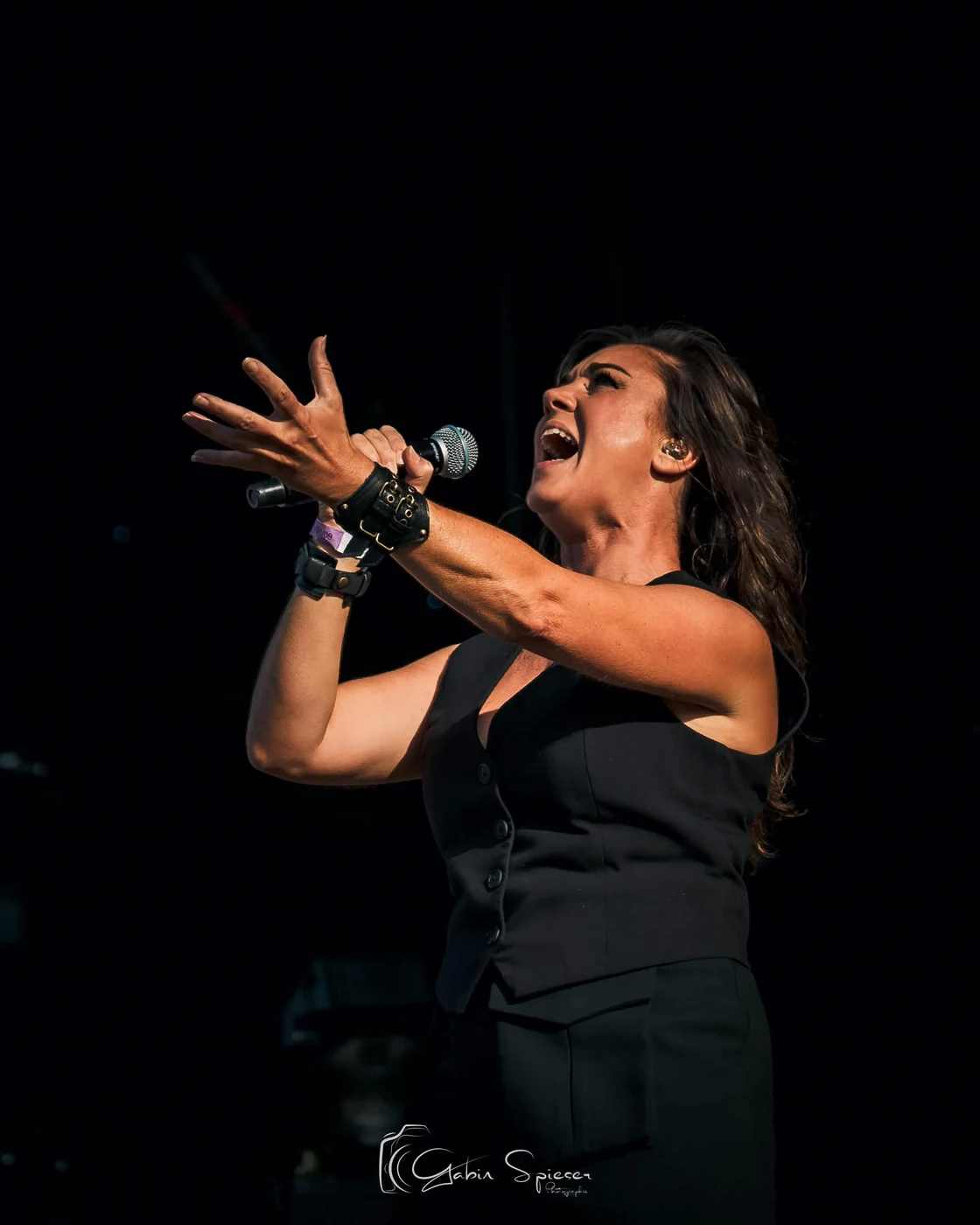 Virginie Rohart — Une chanteuse en tenue noire chante à pleine voix, la main tendue devant elle.